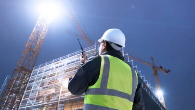 A construction worker speaks into his walkie-talkie as he looks up at a crane that towers over an unfinished building.