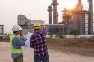 Two industrial professionals examining schematics outside of an industrial plant.