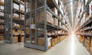A large distribution center with rows of metal racking and vertical storage. Boxes and pallets are stretch wrapped.