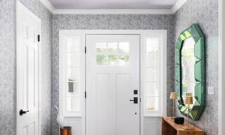 A bright mudroom entryway with different patterns on the brown side table, purple rug, and gray wallpaper.