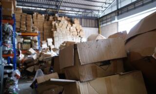 A poorly organized warehouse filled to the brim with haphazardly stacked cardboard boxes and bags.