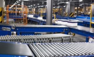 A factory roller conveyor system transporting crates. The conveyors are blue with silver metal rollers.