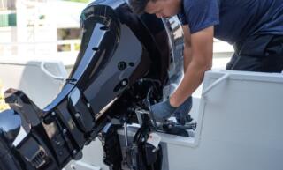 A mechanic is crouched over the stern of a boat, carefully handling tools to install a shiny, new speed boat engine.