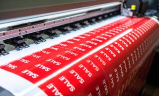 Close-up of a wide-format printer producing a huge sheet of red stickers that all say the word "SALE".