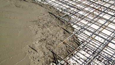 A close-up of concrete being poured over a metal frame made with rebar. There is a wooden form on the outer edge.
