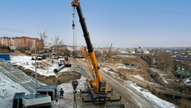 A large yellow and black crane firmly rooted to the dirt ground of a construction site. The hook is lifting up a large chain.
