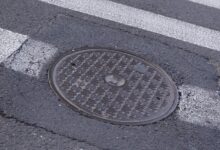 A manhole cover sits on a manhole hole. Thick, white lines surround the manhole cover, indicating a pedestrian crossing.