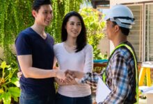 A man and woman stand outside their home talking to a contractor wearing a hard hat. The man shakes the contractor's hand.