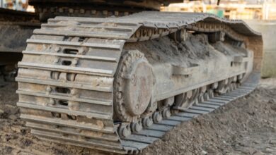 A close-up of a large track pad and rollers on a yellow heavy machine sitting on a pile of dirt and rubble.