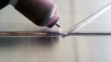 A purple arc flashes between a worn pink TIG welding tip and an aluminum rod held against a metal part.