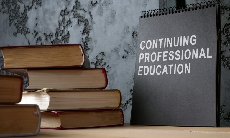 A notepad reading the words "Continuing Professional Education" sits next to several books stacked up on a desk.