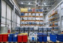 The inside of a storage facility housing drums and IBC tanks of chemicals. Some tanks are stacked on a shelving unit.