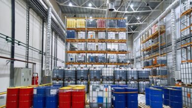 The inside of a storage facility housing drums and IBC tanks of chemicals. Some tanks are stacked on a shelving unit.