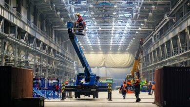 A production warehouse with workers moving around to install new parts. The workers are wearing safety gear.