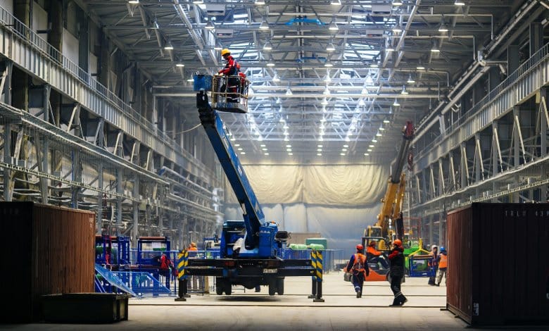 A production warehouse with workers moving around to install new parts. The workers are wearing safety gear.