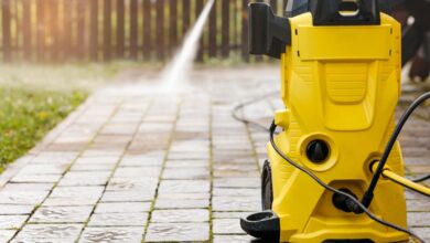 A yellow pressure washer on a brick backyard patio. A person sprays water from the machine in the background.