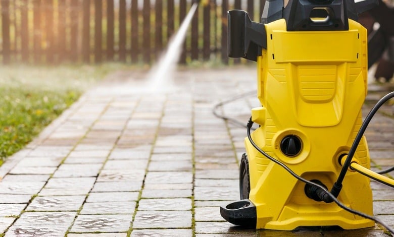 A yellow pressure washer on a brick backyard patio. A person sprays water from the machine in the background.