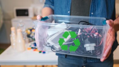 A close-up of a man holding a clear plastic recycling bin that is filled to the top with old electronic devices.