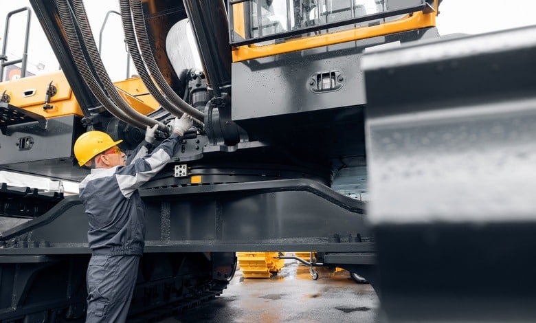 A professional mechanic is inspecting heavy-duty equipment on an excavator to aid in progressing the work.