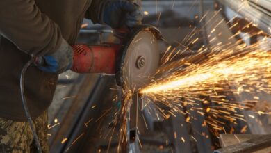 A close-up of a man is using a power blade tool to cut metal. There are sparks flying off of the metal.