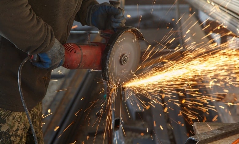 A close-up of a man is using a power blade tool to cut metal. There are sparks flying off of the metal.