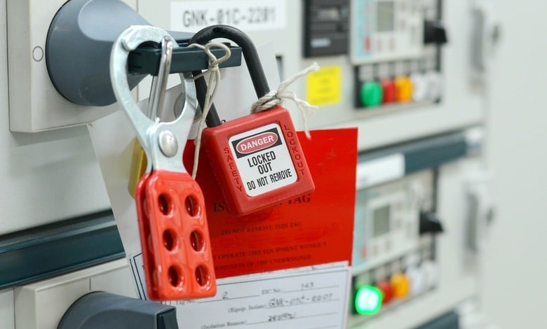 A close-up of a section of industrial electrical equipment. A red padlock attached to a handle reads "Danger: Locked Out."