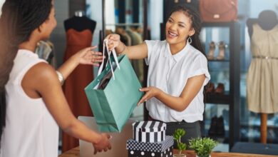 Two women are standing across from one another. The woman on the right is handing the woman on the left a bag.