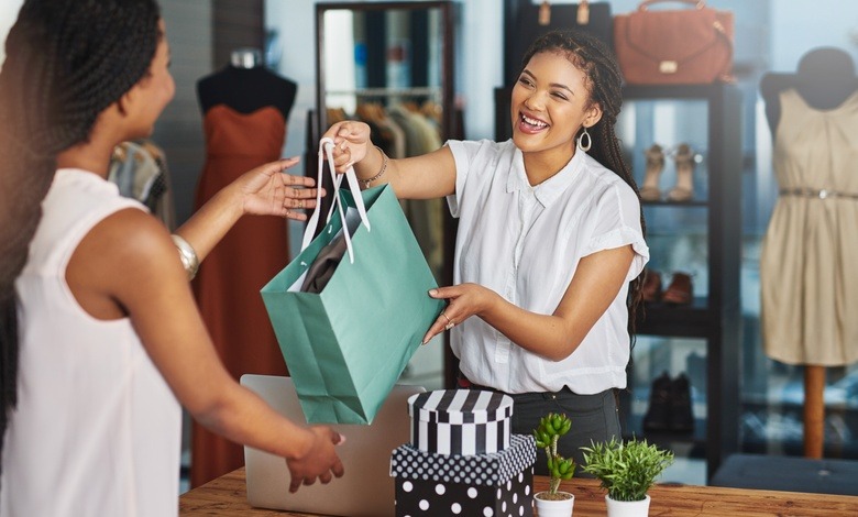 Two women are standing across from one another. The woman on the right is handing the woman on the left a bag.