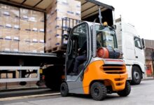 A forklift is lifting and unloading items from a semi-truck at a company's shipping docking station.