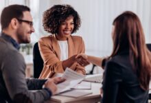 Three people at a table together for a job interview. Two of them are smiling as the candidate shakes a woman's hand.