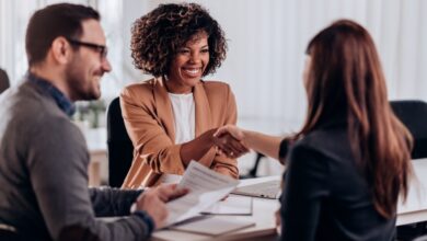 Three people at a table together for a job interview. Two of them are smiling as the candidate shakes a woman's hand.