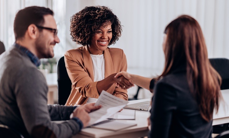 Three people at a table together for a job interview. Two of them are smiling as the candidate shakes a woman's hand.