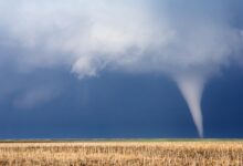A small tornado cutting through some farm fields. The crops have already been harvested from this area.