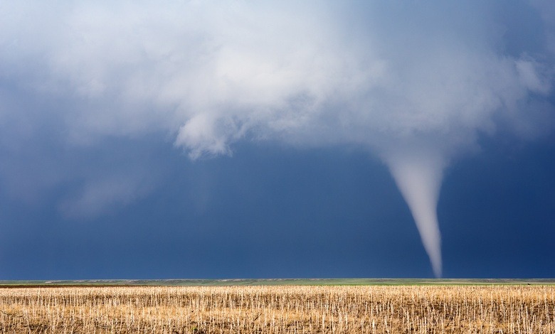 A small tornado cutting through some farm fields. The crops have already been harvested from this area.
