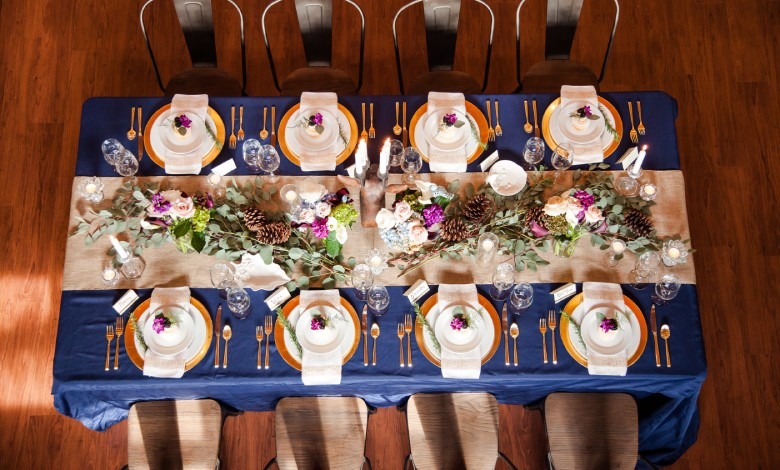 An overhead angle of a rectangular table. The table has a navy tablecloth, a beige runner, and gold chargers.