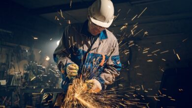 A man wearing a helmet, safety gloves, and a uniform with thick fabric, using a grinder producing multiple sparks.