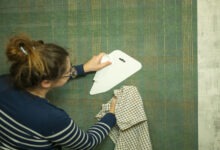 A person holding a rag and using a spatula to smooth wallpaper at home. The wallpaper is green with golden lines.