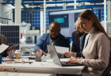 A group of people at a business sitting at a desk with laptops and various office supplies in front of them.