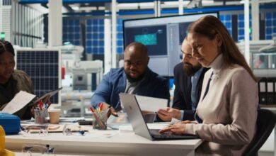 A group of people at a business sitting at a desk with laptops and various office supplies in front of them.