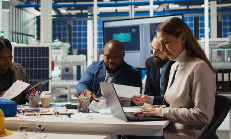 A group of people at a business sitting at a desk with laptops and various office supplies in front of them.