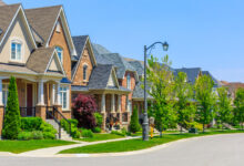 A row of houses with greenery in front on the lawns. There is a streetlamp in the center of frame.