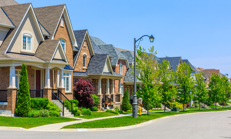A row of houses with greenery in front on the lawns. There is a streetlamp in the center of frame.