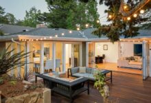 The patio of a modern home with hardwood floors, two loveseat sofas, string lights, and open foldable doors to the house.