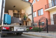 A truck packed with items is parked in front of a house. The truck is white and the house is made out of brick.