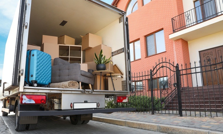 A truck packed with items is parked in front of a house. The truck is white and the house is made out of brick.