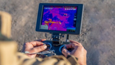 A person is operating a drone with a thermal camera. The controller has a screen displaying pink, red, and yellow objects.