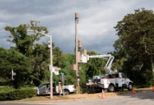 A fiber contract crew with their white work truck hoisted to an electrical pole. One engineer is working on the lines.