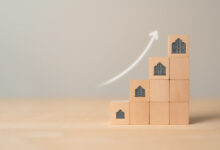 10 wooden blocks arranged as a staircase, the outer four with images of buildings on them. A nearby digital arrow sweeps upward.